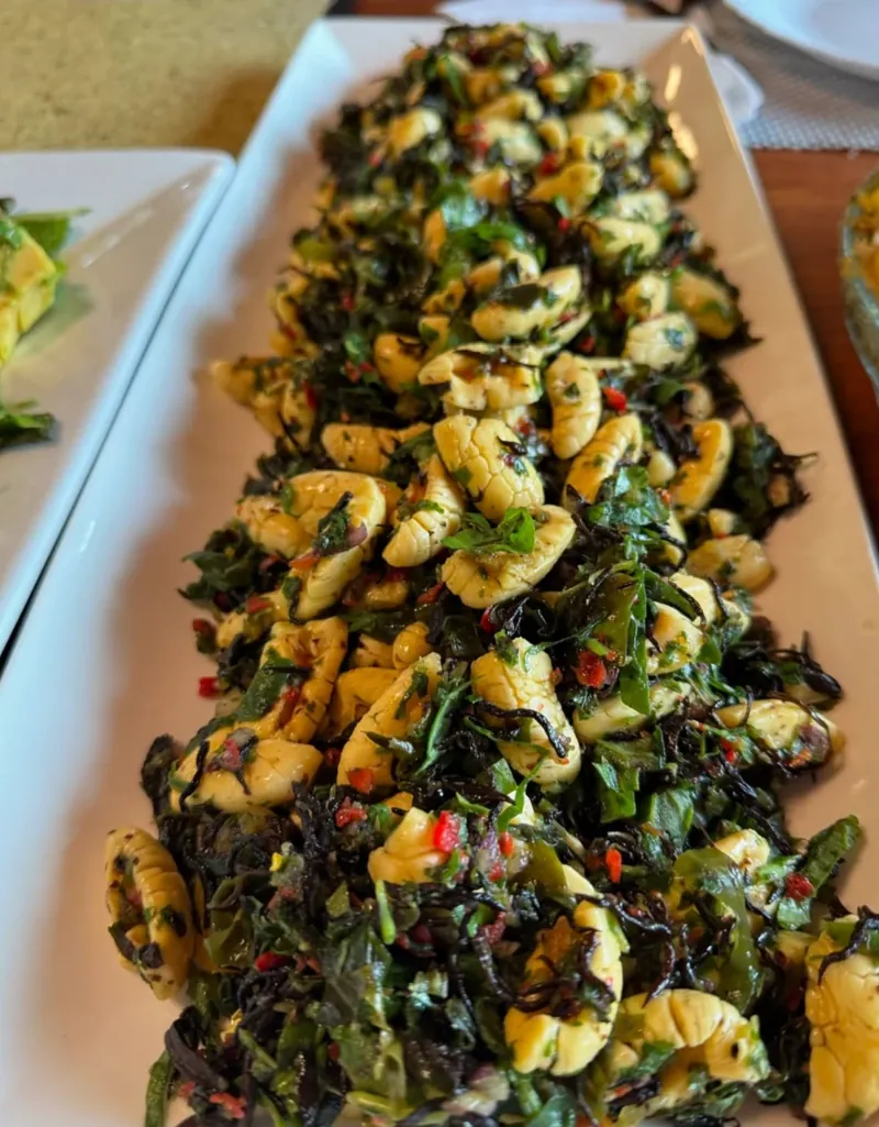 A long white platter of ackee with greens, sea vegetables and red pepper.