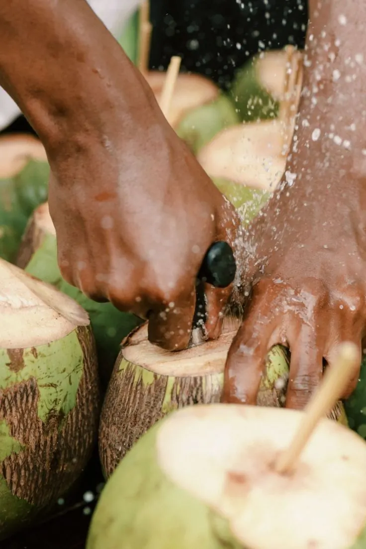 Hands opening a green coconut with a knife, water splashing.